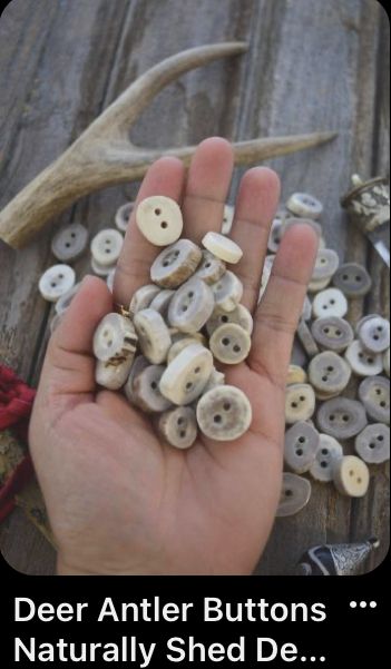 a hand is holding some buttons in front of deer antlers