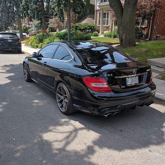 a black mercedes cls parked on the street in front of some trees and houses