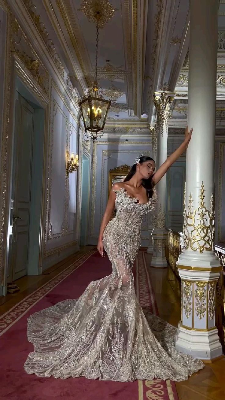 a woman in a dress standing on a red carpet next to a white column and chandelier