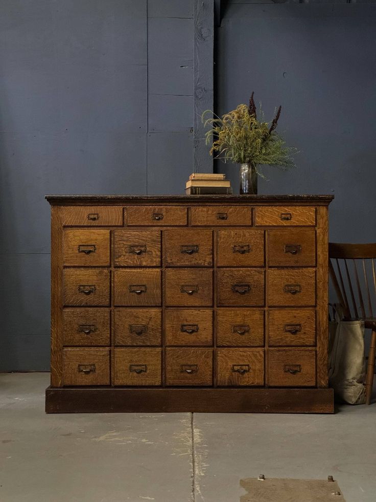 an old wooden dresser with many drawers and a plant on top, in front of a blue wall