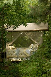 a bed in the middle of some trees with a canopy over it's head