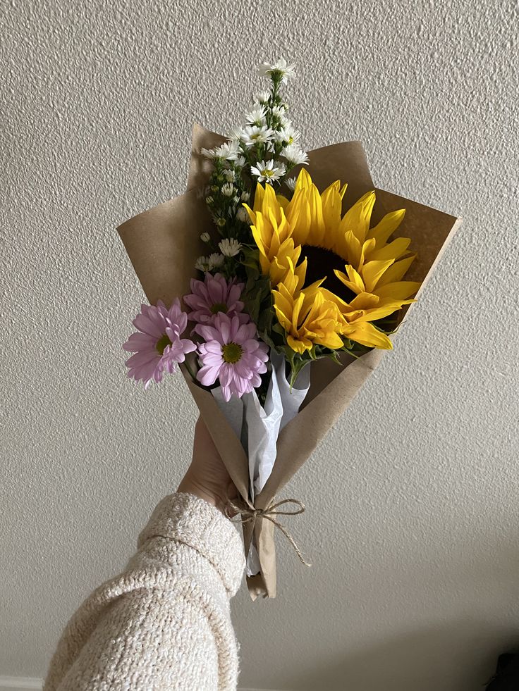 a person holding a bouquet of flowers in their hand with the sunflowers and daisies tied to it