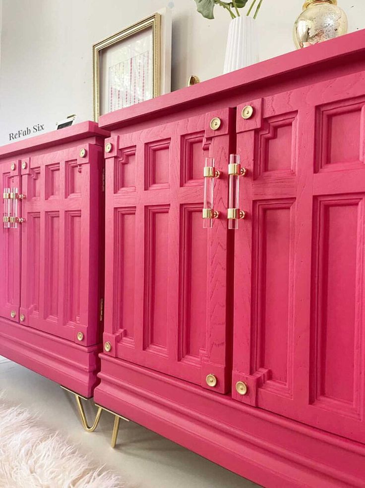 a pink dresser with gold handles and knobs on it's doors, in a living room