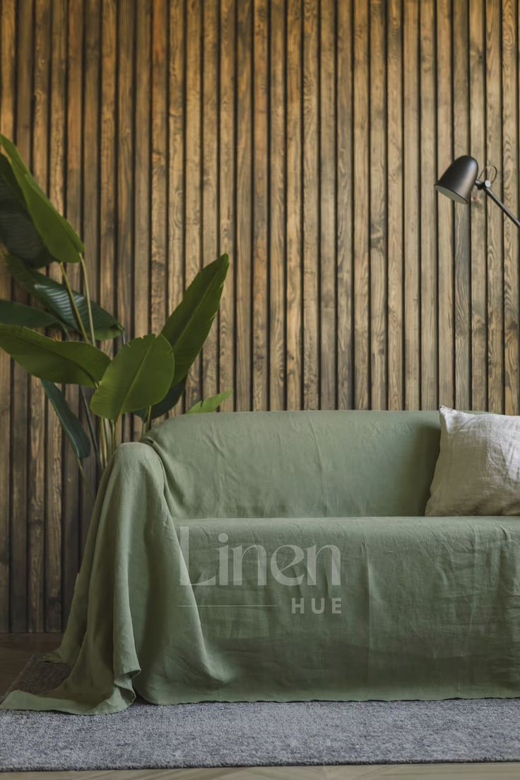 a green couch sitting next to a lamp on top of a wooden floor covered in a blanket