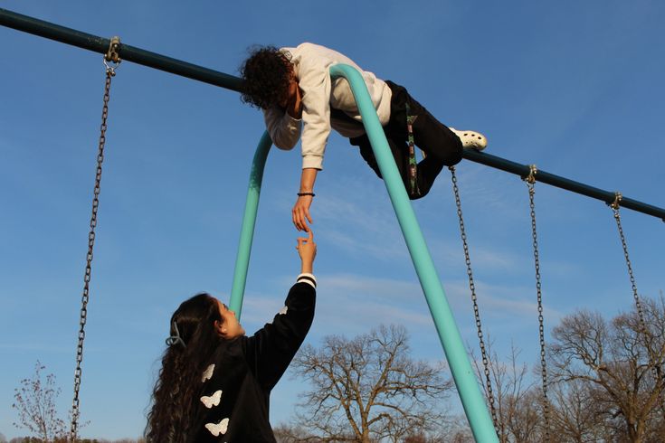 two women are climbing on the ropes in an outdoor playground area with trees and blue sky behind them