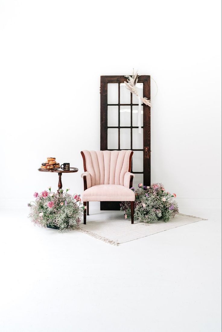 a pink chair sitting in front of a mirror on top of a white floor next to potted plants