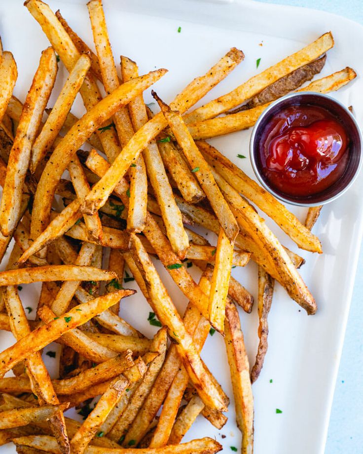 french fries with ketchup and mustard on a white platter next to dipping sauce