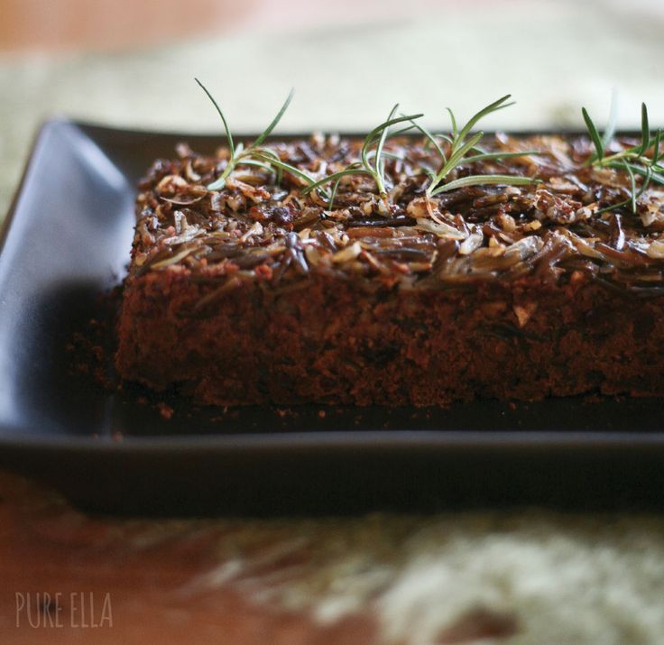 a black plate topped with brownies covered in nuts and herbs on top of a wooden table