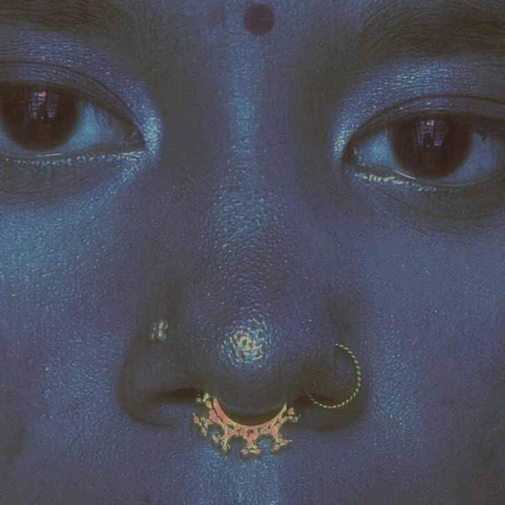 a close up of a person's face with blue paint on it and a nose ring