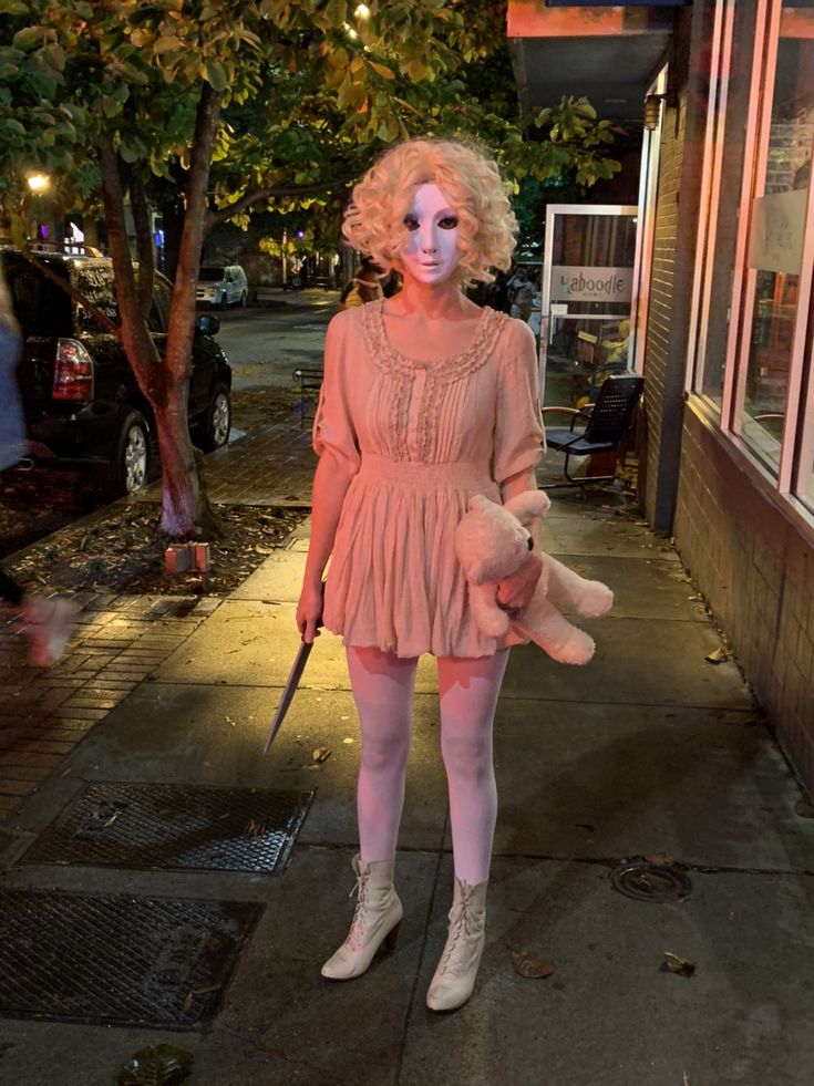 a woman dressed in pink holding a teddy bear and walking down the street at night