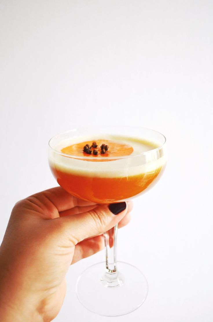 a hand holding a wine glass filled with orange liquid and garnished with blackberries