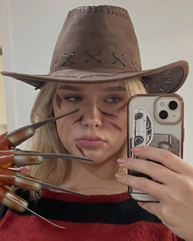 a woman wearing a cowboy hat and holding a cell phone with nails on her face