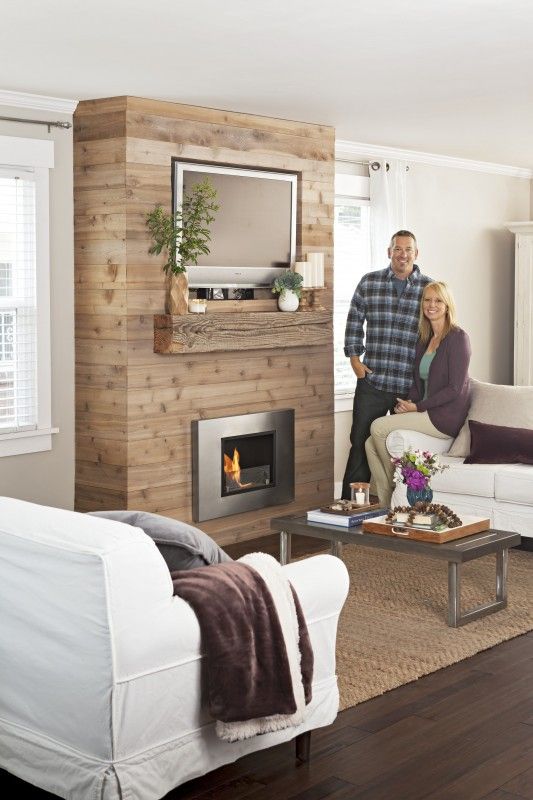 a man and woman standing next to each other in a living room with a fireplace