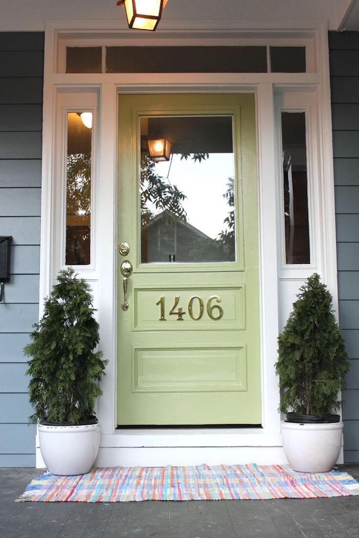 a green front door with two potted plants on the side and a light fixture above it