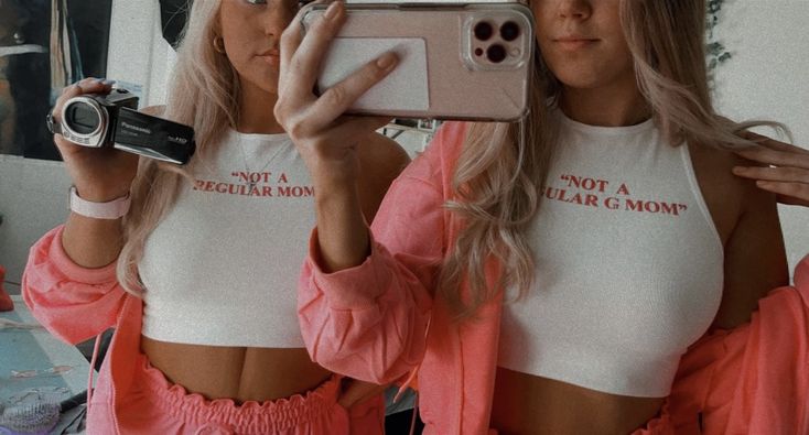 two women taking a selfie in front of a mirror wearing matching shirts and shorts