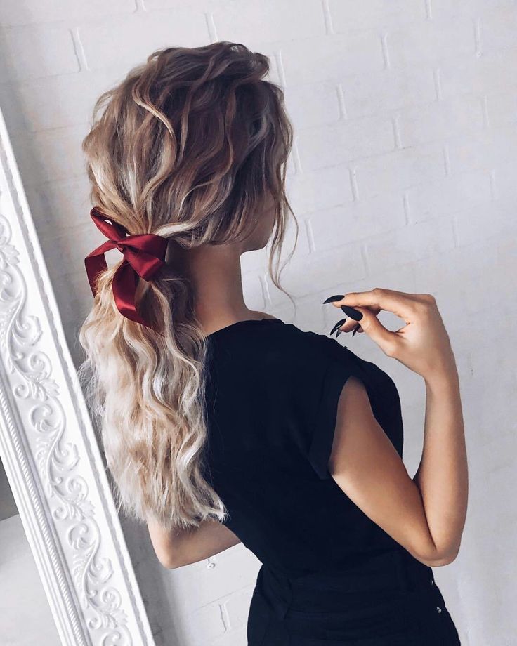 a woman with long blonde hair and a red bow in her ponytail is looking at herself in the mirror