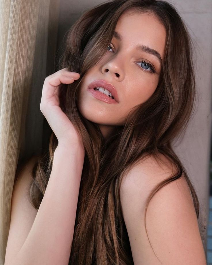 a beautiful young woman leaning against a wall with her hand on her head and looking at the camera