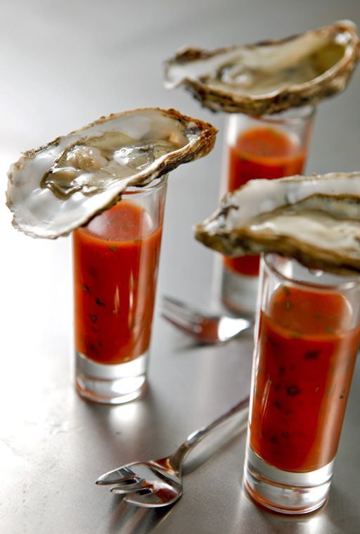 three glasses filled with sauce and oysters on a table next to silver utensils