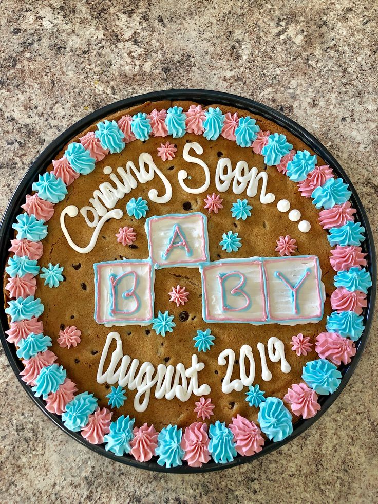 a baby announcement cake is decorated with pink, blue and white frosting on a black plate