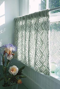 a white curtain hanging from the side of a window next to a vase with flowers