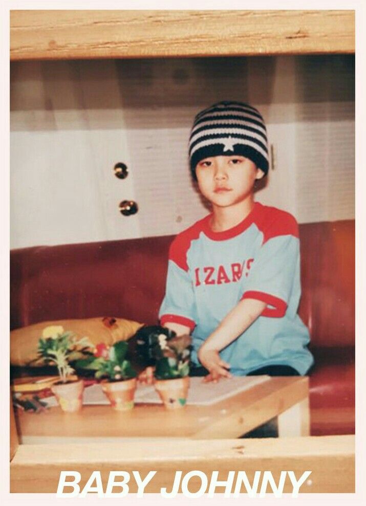 a young boy sitting on top of a wooden table next to a potted plant