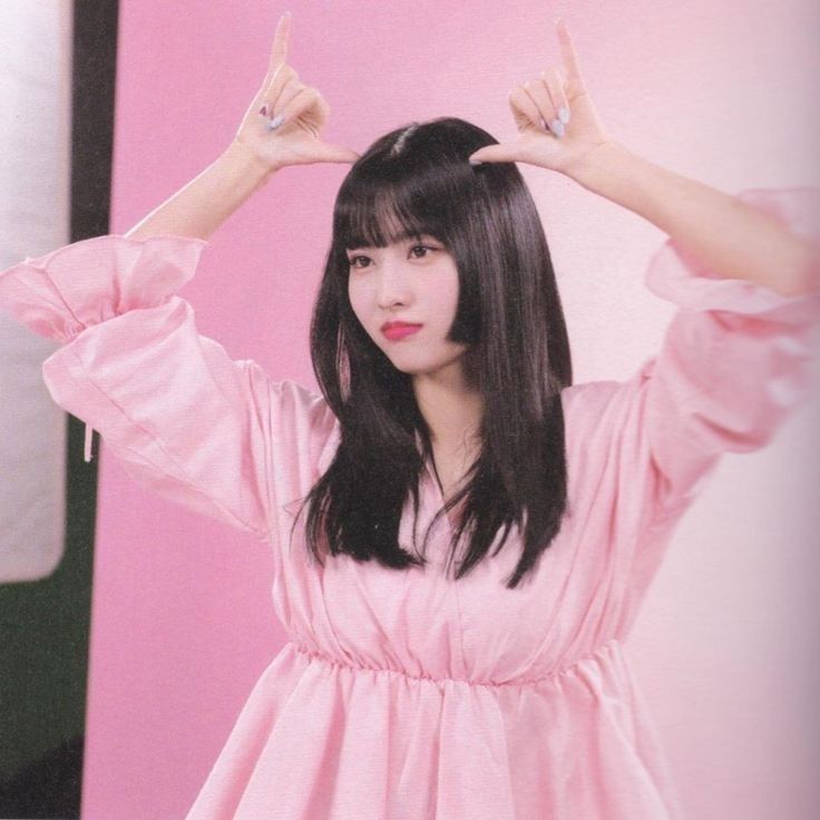 a woman with long black hair wearing a pink dress and holding her hands up in the air