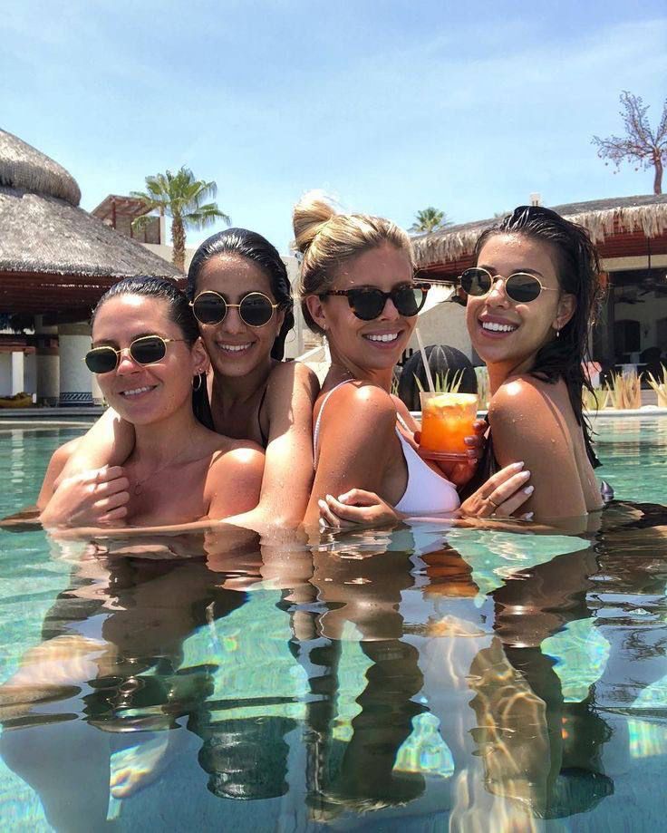 three beautiful women sitting in the middle of a swimming pool holding drinks and smiling at the camera