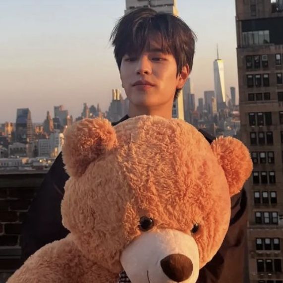 a young man holding a large teddy bear in front of a cityscape with skyscrapers