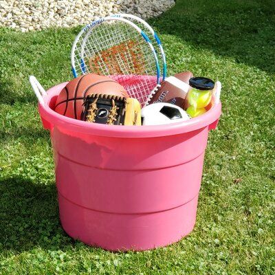 a pink bucket filled with sports equipment on top of a grass covered field next to a tennis racquet