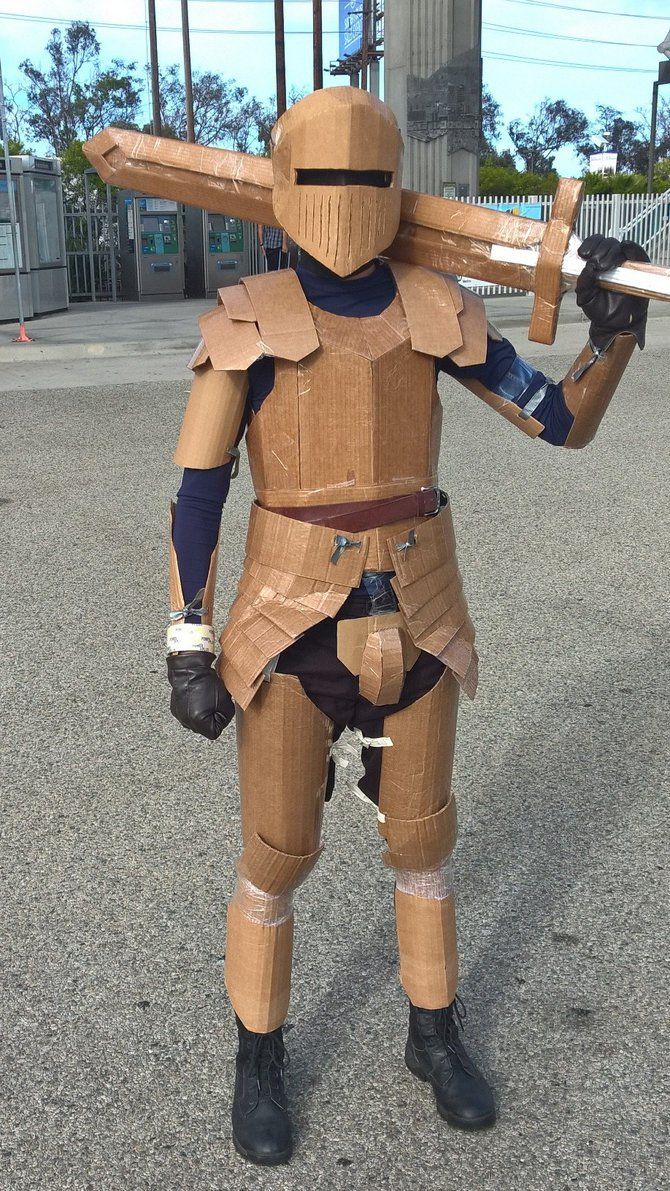 a cardboard man dressed in armor and holding two swords, standing on the street with his arms stretched out