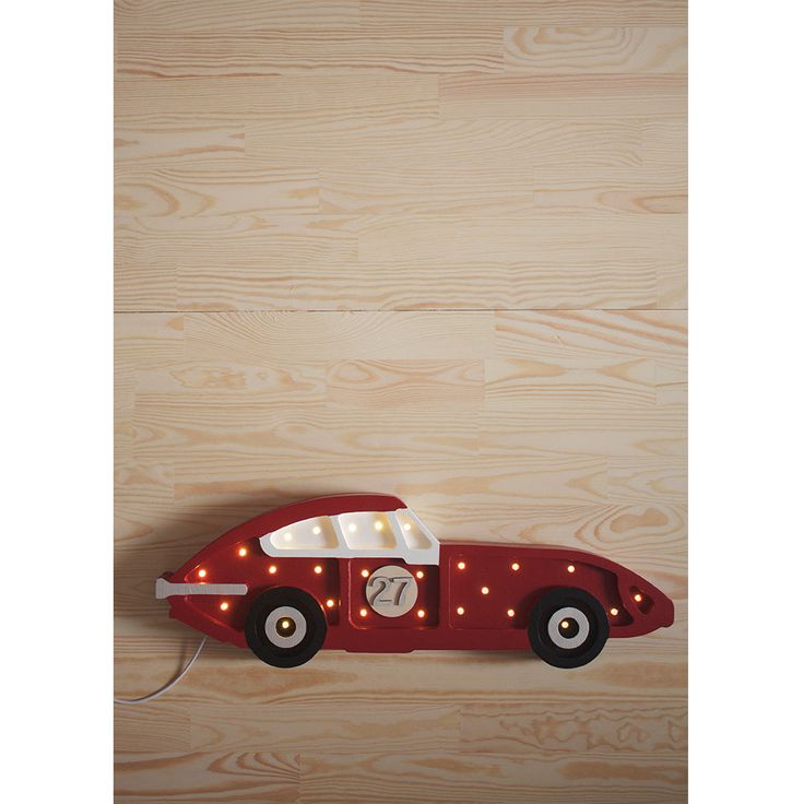 a red toy car with lights on the front and side, attached to a wooden wall