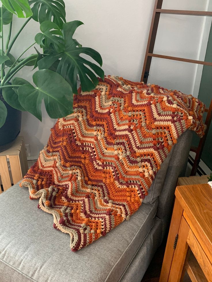 a crocheted blanket sitting on top of a couch next to a potted plant