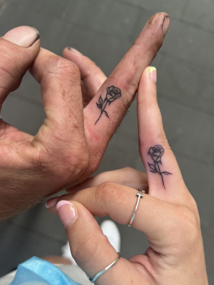 two people with tattoos on their fingers making the letter v and one holding a rose