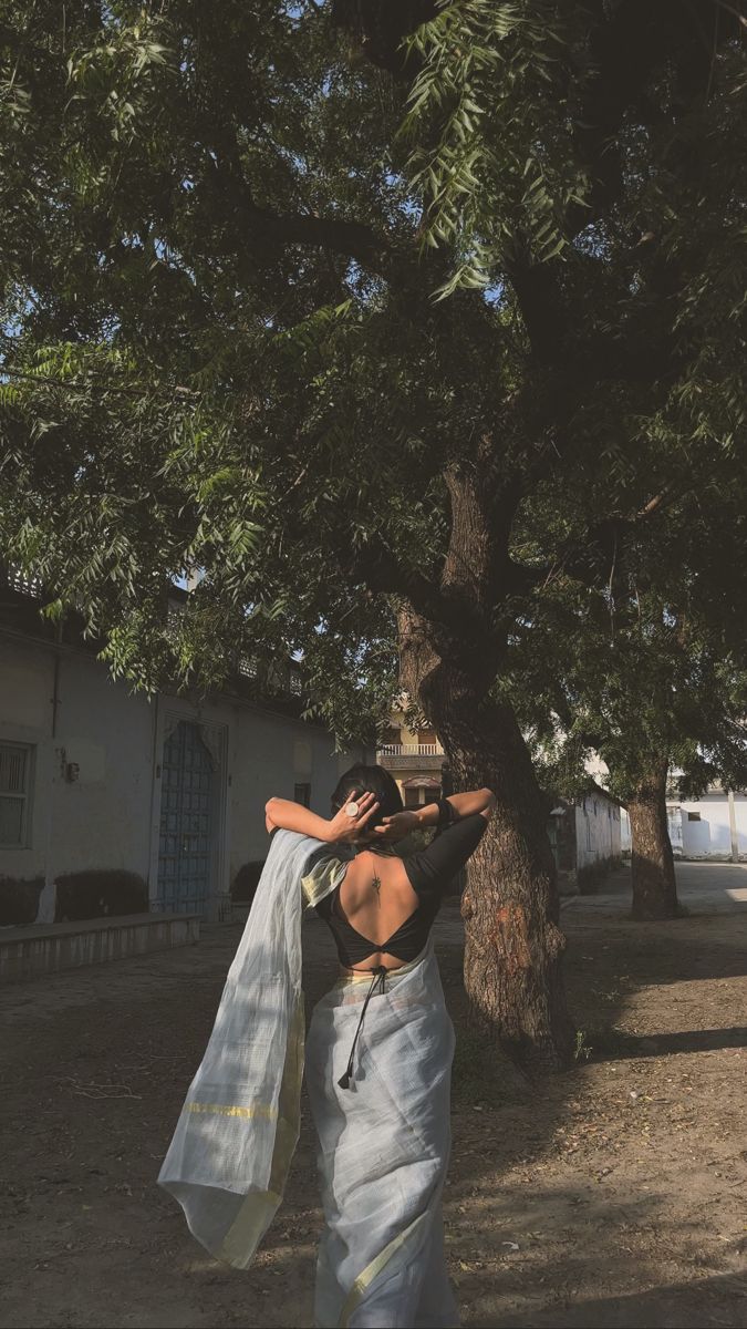 a woman standing under a tree with a white sari on her head and one hand in the other's pocket