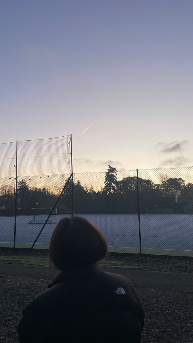 a person sitting in front of a tennis court at sunset with the sun going down