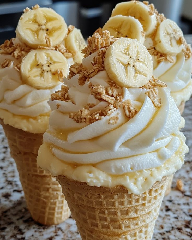 three ice cream cones with banana slices and nuts on top, sitting on a table