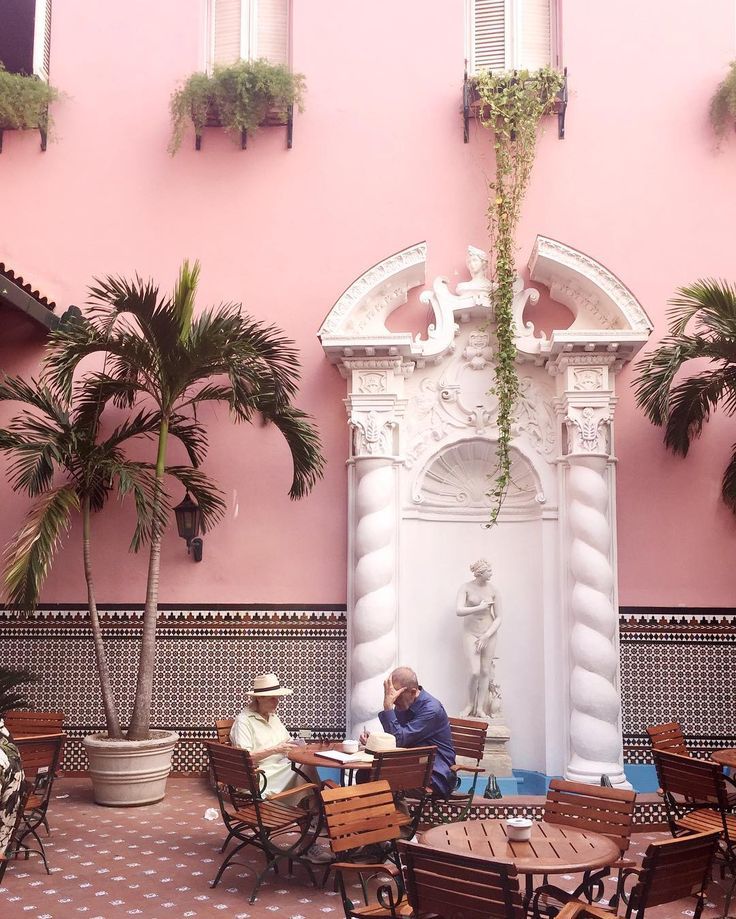 two people sitting at tables in front of a fountain with palm trees and potted plants