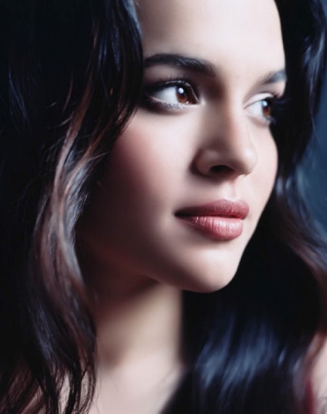 a woman with long black hair and blue eyes posing for a photo in front of a dark background