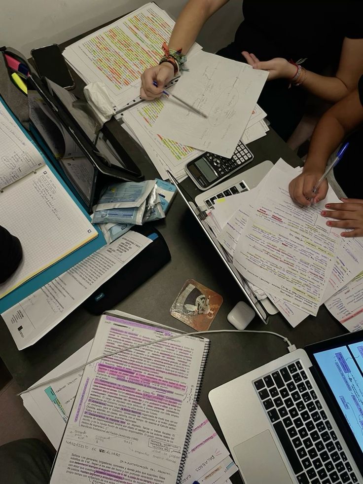 several people sitting at a table with laptops and papers on top of each other