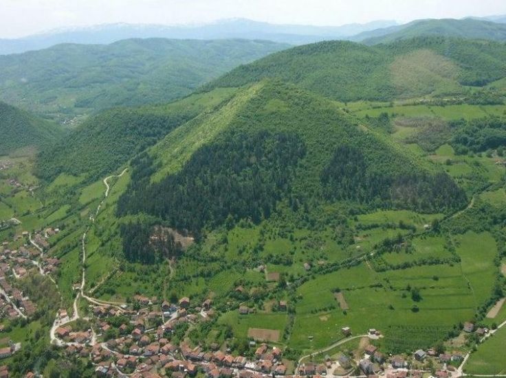 an aerial view of a small village in the middle of a green valley surrounded by mountains