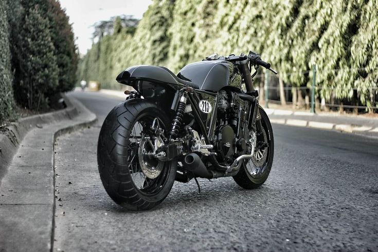 a black motorcycle parked on the side of a road next to bushes and trees in front of it