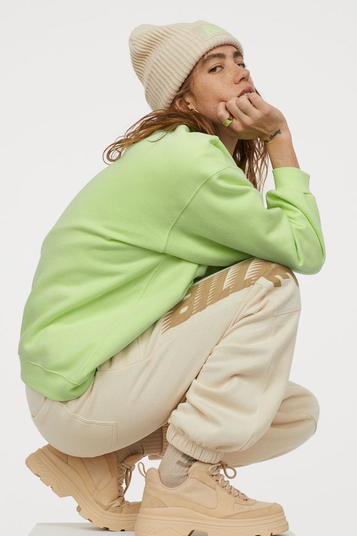 a woman sitting on the ground with her hand under her chin, wearing a green sweater and khaki pants