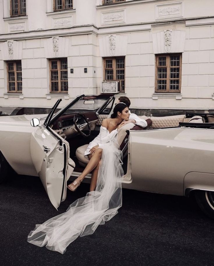 a woman sitting in the back of a car with her dress draped over it's side