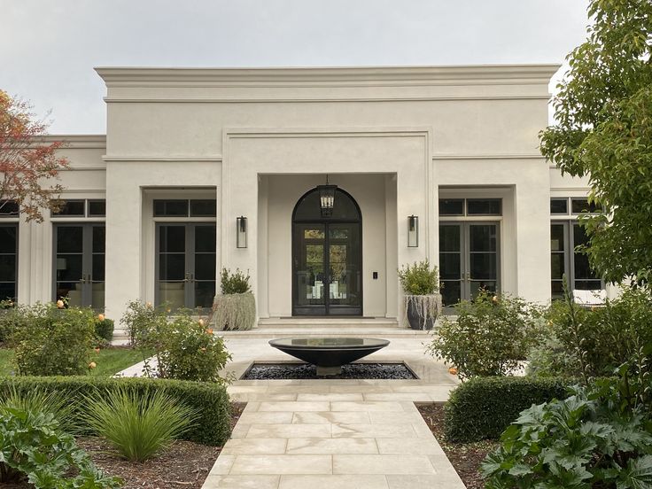 a large white house with a fountain in the front yard and lots of greenery