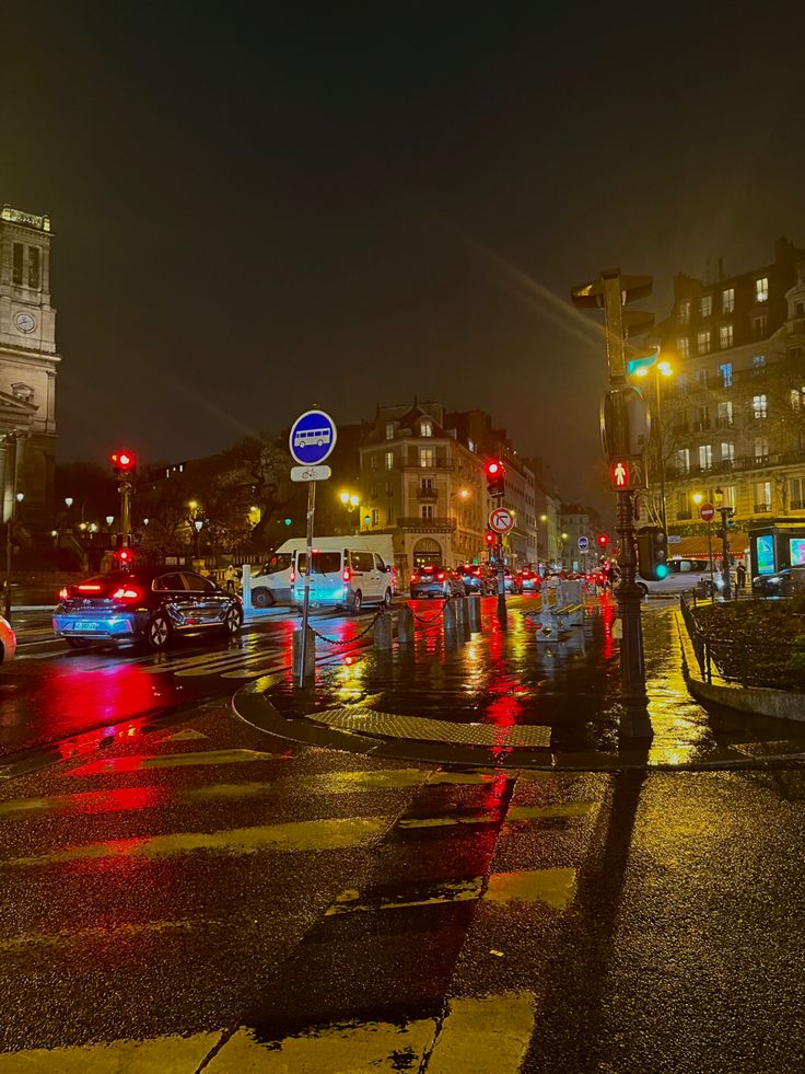 a city street at night with traffic lights and buildings in the background on a rainy day