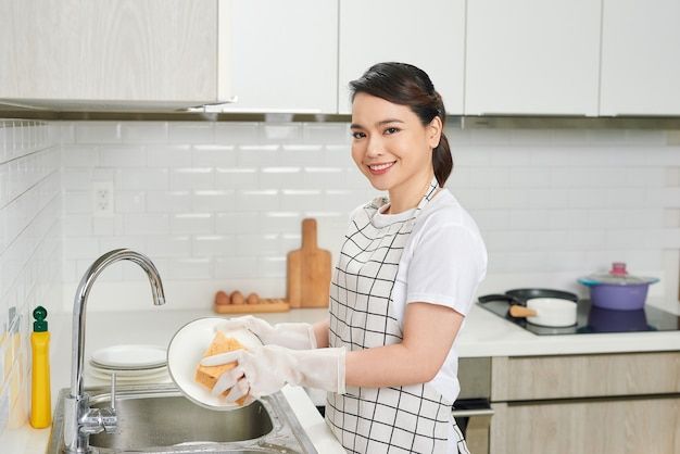 a woman in an apron is washing dishes on the sink and smiling at the camera