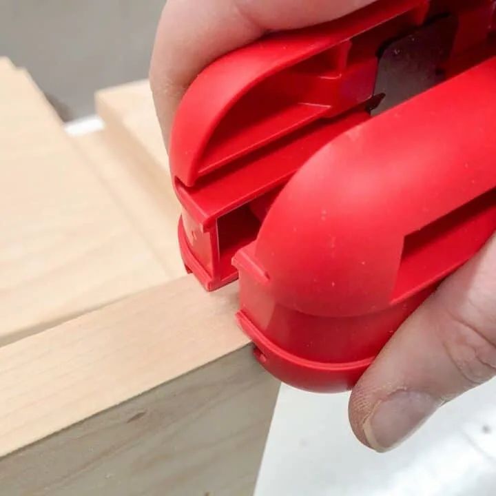 a hand holding a red plastic object in it's right hand and another piece of wood behind it