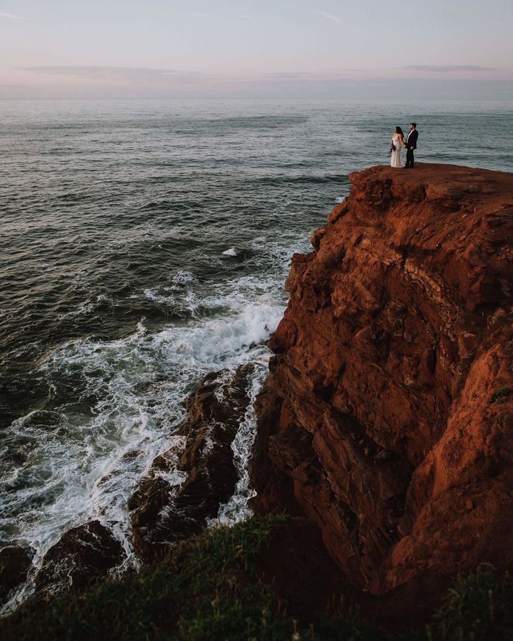 a couple standing on top of a cliff next to the ocean