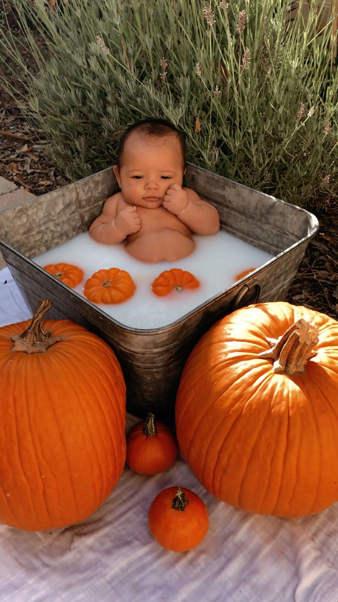 a baby in a bath surrounded by pumpkins