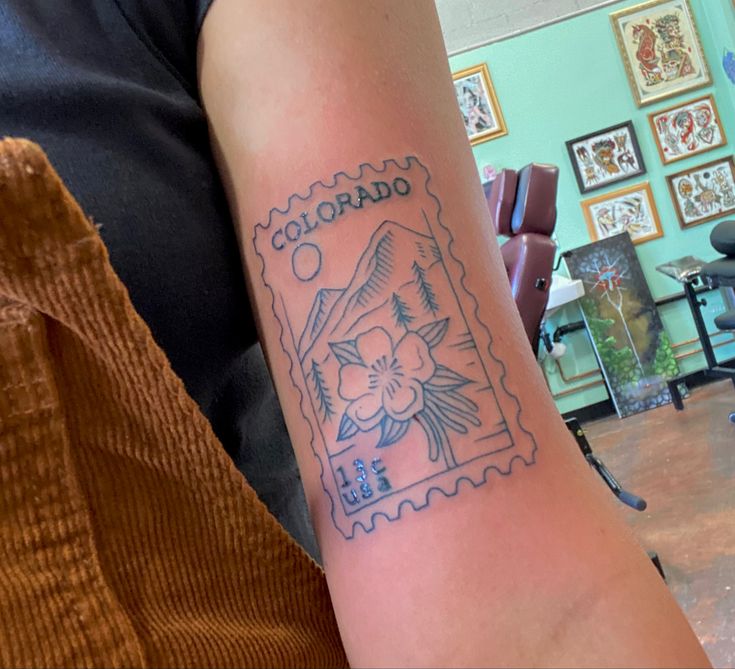 a person with a tattoo on their arm that reads colorado and has flowers in the stamp